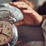 Shot of a young man reaching for his alarm clock after waking up in bed at home