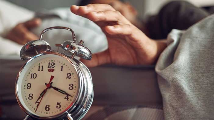 Shot of a young man reaching for his alarm clock after waking up in bed at home